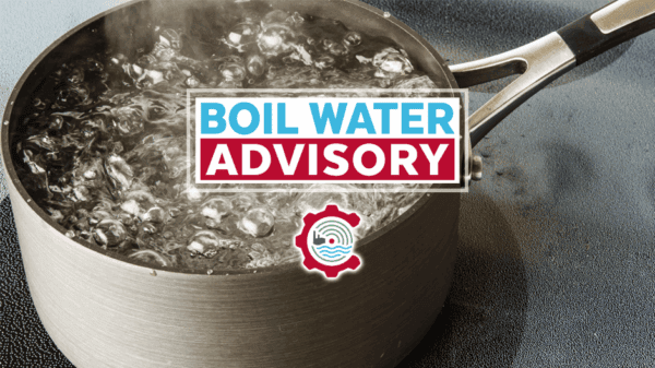 A pot of water boiling on a stove with a sign that reads Boil Water Advisory overlaid on the image.