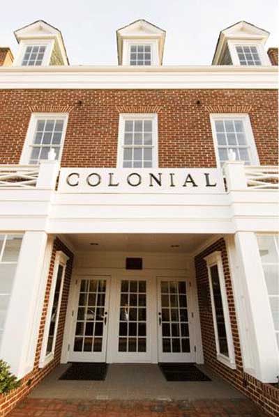 Brick building with large windows and a white entrance. The word COLONIAL is displayed above the doors. Three dormer windows are visible on the roof.