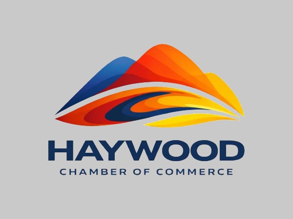Logo of Haywood Chamber of Commerce, featuring stylized, layered mountain shapes in blue, orange, red, and yellow above the organizations name on a gray background.