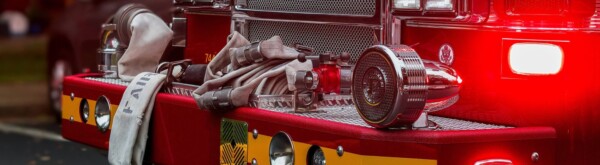 Close-up of the front of a fire truck with coiled fire hoses, a metal nozzle, and a red emergency light illuminated.