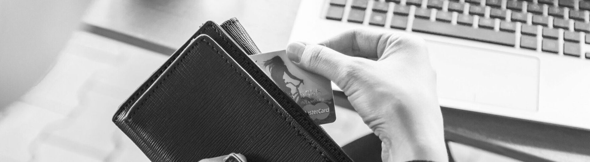 A person holding a wallet and pulling out a credit card in front of a laptop.