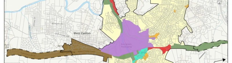 A city map with colored regions: brown, green, purple, yellow, orange, and red, indicating different zoning or planning areas. Streets and rivers are also depicted, with labeled neighborhoods and boundaries.
