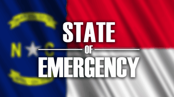 North Carolina flag background with bold white text reading STATE OF EMERGENCY across the center.