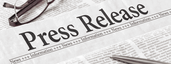 A newspaper with the bold headline Press Release, eyeglasses, and a pen resting on the paper.