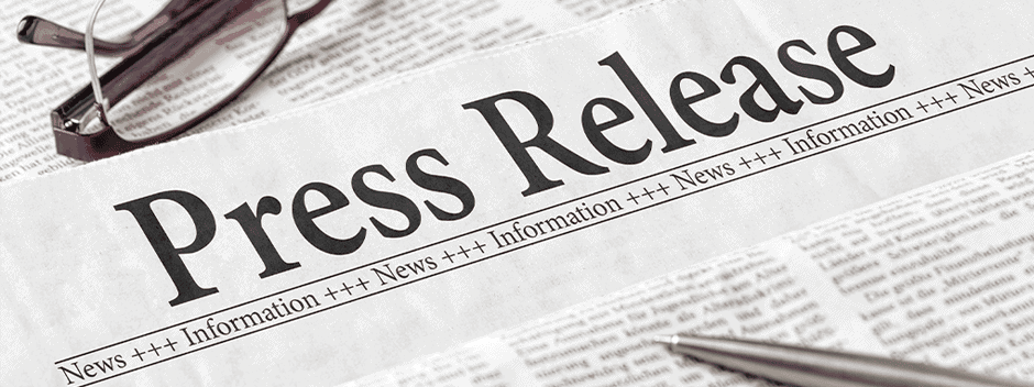A newspaper with the bold headline Press Release, eyeglasses, and a pen resting on the paper.