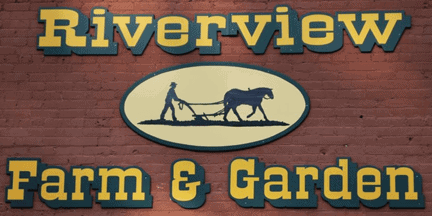 A sign reading Riverview Farm & Garden with an oval graphic of a person plowing a field with a horse, all set against a brick wall background.