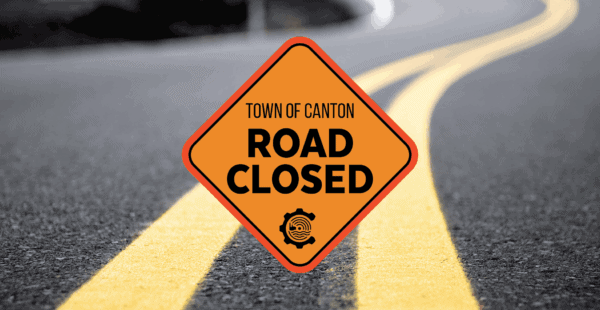 Orange diamond Road Closed sign with Town of Canton text is centered on a road with double yellow lines. The road curves and fades into the background.