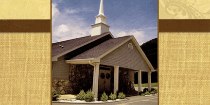 Small church building with a steeple, stone and siding exterior, double doors, and landscaped bushes at the entrance, under a partly cloudy sky.