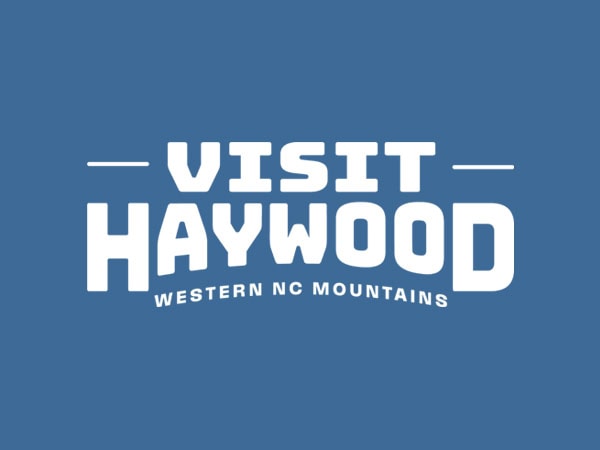 White text on a blue background reads Visit Haywood with Western NC Mountains underneath in smaller letters.