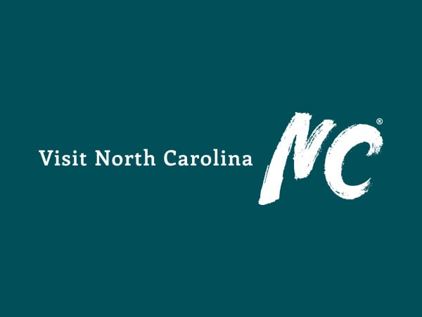 Teal background with the words Visit North Carolina in white, followed by large, stylized white letters NC to the right.